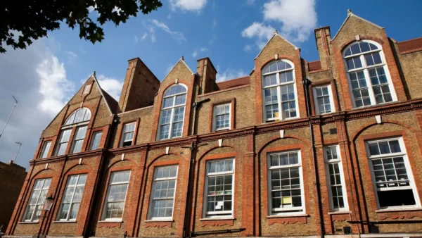 A multi-story brick school building with large arched and rectangular windows under a blue sky.
